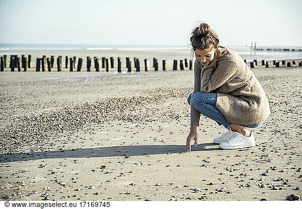 Junge Frau in hockender Position auf Sand am Strand
