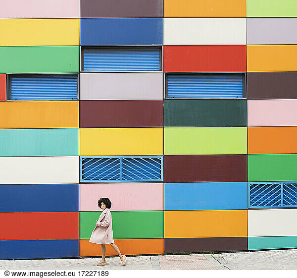 Junge Frau in Jacke geht an einem mehrfarbigen Gebäude vorbei