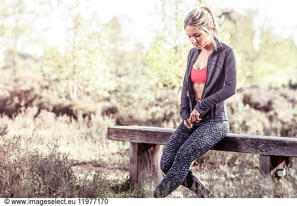 Junge Frau in ländlicher Umgebung  auf Bank sitzend  Sweatshirt mit Reißverschluss