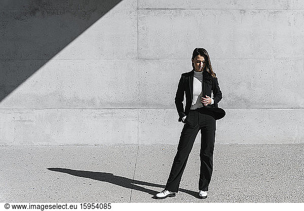 Junge Frau in schwarzem Anzug vor Betonmauer stehend