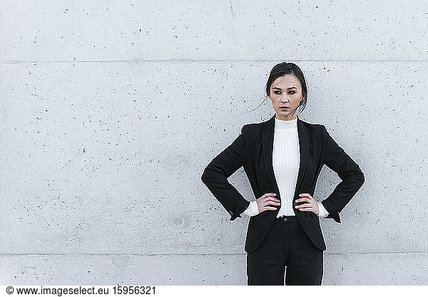 Junge Frau in schwarzem Anzug vor Betonmauer stehend