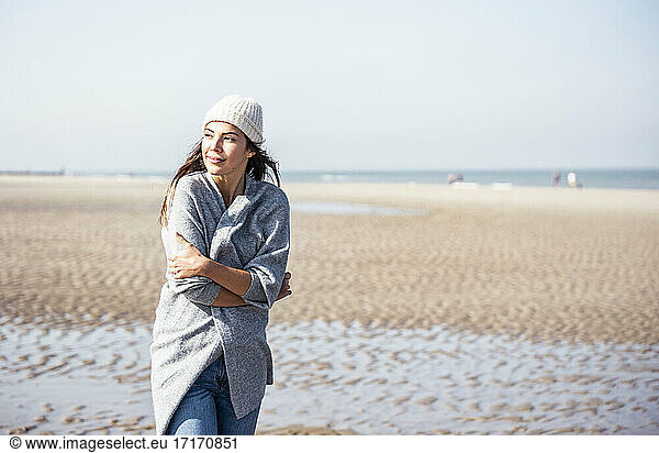Junge Frau in Strickjacke beim Strandspaziergang nachdenklich