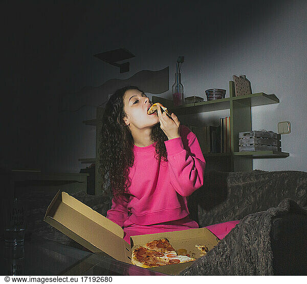 junge Frau isst Pizza auf dem Sofa und sieht sich einen Film an