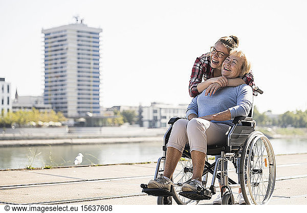 Junge Frau Kopf an Kopf mit ihrer lachenden Großmutter im Rollstuhl sitzend