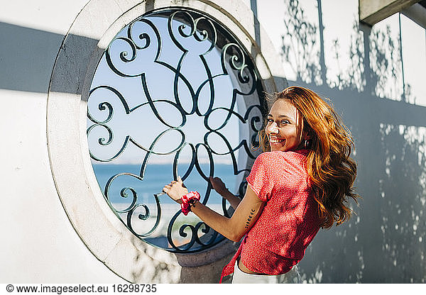Junge Frau lächelt  während sie ein Fenstergitter in Alfama  Lissabon  Portugal hält