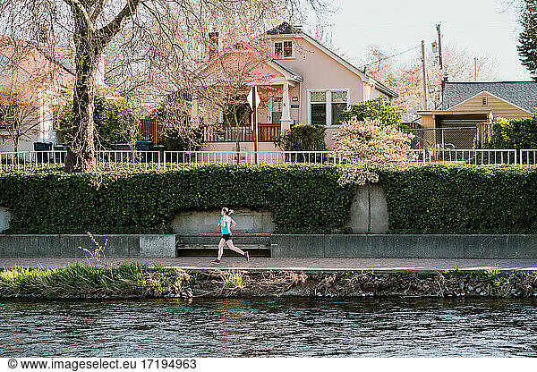 Junge Frau läuft entlang des Flusses mit Häusern und Bäumen im Hintergrund