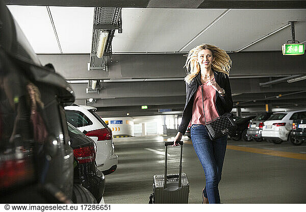 Junge Frau läuft mit Rollkoffer auf einem Flughafenparkplatz