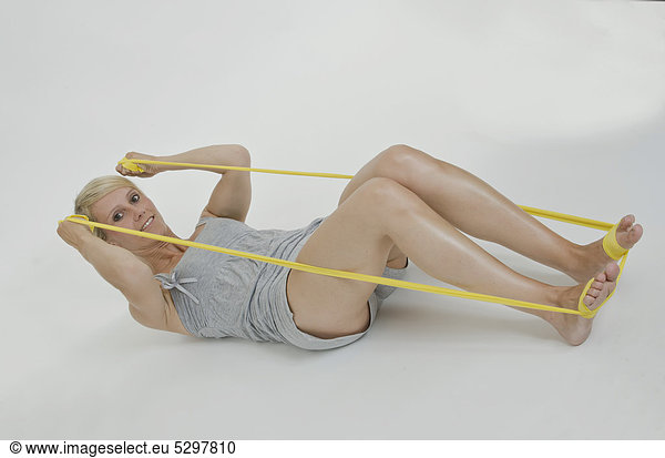 Junge Frau liegend mit gelbem Gymnastikband um die F¸_e  zieht mit den H‰nden