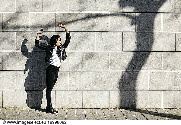 Junge Frau macht Schatten auf einer weißen Wand mit einem Schatten eines Baumes