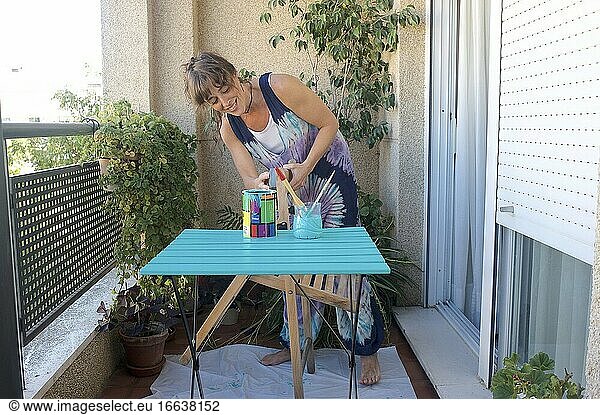 Junge Frau malt einen Stuhl mit grüner Farbe auf ihrer Terrasse