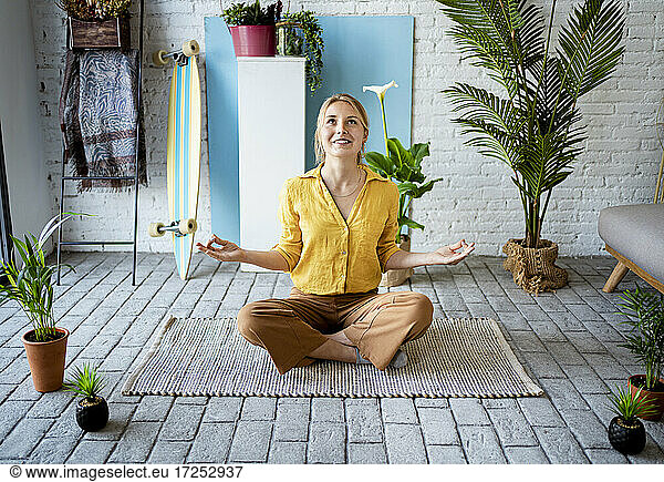 Junge Frau meditiert zu Hause auf einer Matte sitzend