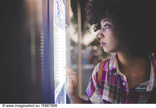 Junge Frau mit Afro-Frisur benutzt einen Touchscreen-Automaten in der Stadt