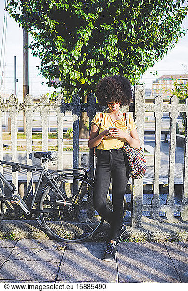 Junge Frau mit Afro-Frisur benutzt Smartphone in der Stadt