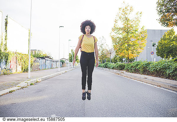 Junge Frau mit Afro-Frisur springt auf eine Straße in der Stadt