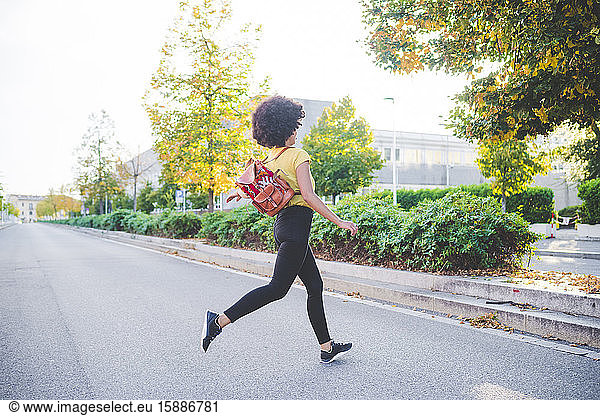 Junge Frau mit Afrofrisur rennt auf einer Straße in der Stadt