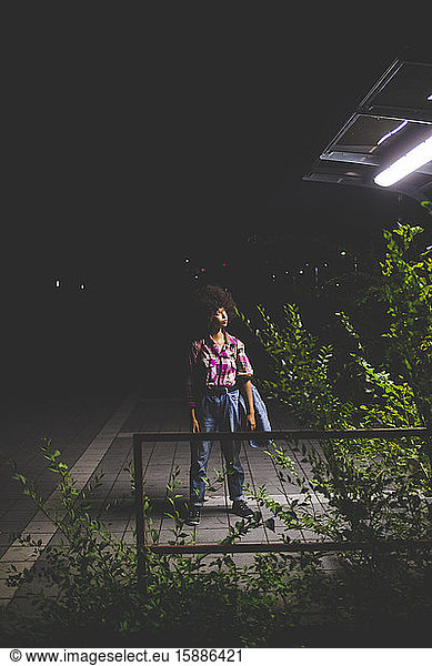 Junge Frau mit Afrofrisur steht nachts auf Bahnsteig