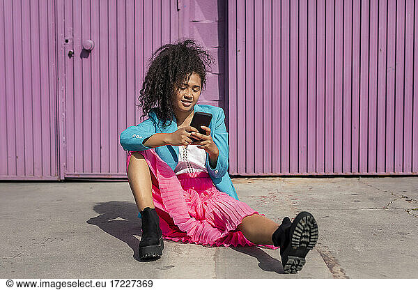 Junge Frau mit Afrofrisur telefoniert auf dem Gehweg sitzend