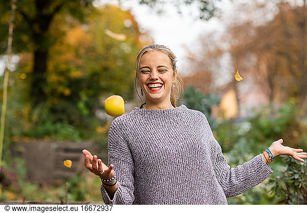 Junge Frau mit blondem Haar spielt mit Apfel in einem städtischen Garten