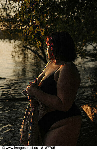 Junge Frau mit Handtuch am Wasser stehend bei Sonnenuntergang