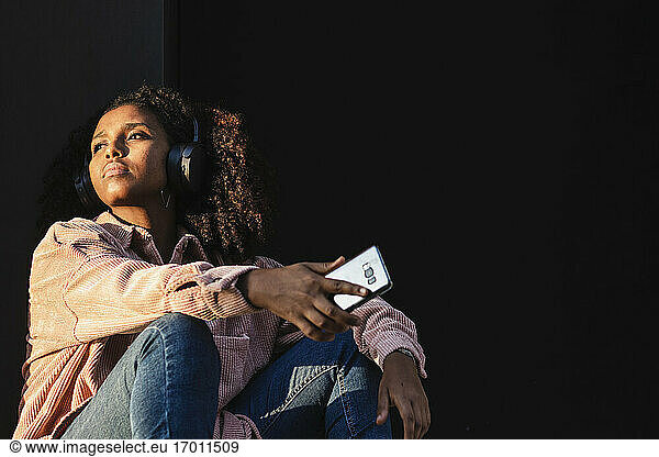 Junge Frau mit Handy Tag träumt gegen schwarze Wand auf sonnigen Tag