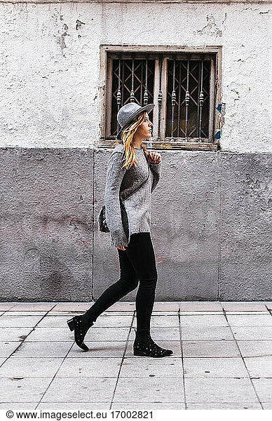 Junge Frau mit Hut geht an einem Gebäude vorbei auf die Straße