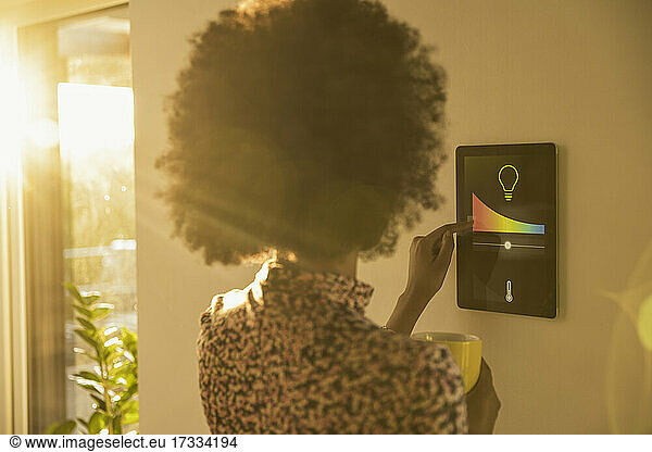 Junge Frau mit Kaffeetasse  die die Temperatur am Hausautomatisierungsgerät kontrolliert