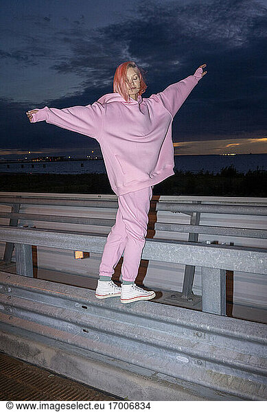 Junge Frau mit rosa Haaren und rosa Trainingsanzug steht nachts auf einer Straßenschranke