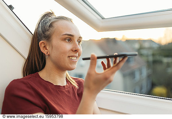 Junge Frau mit Smartphone am Fenster im Gegenlicht