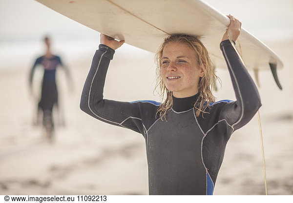 Junge Frau mit Surfbrett auf dem Kopf am Strand