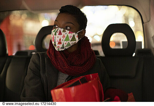 Junge Frau mit weihnachtlicher Gesichtsmaske auf dem Rücksitz eines Taxis