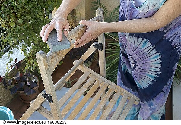 Junge Frau schleift einen Stuhl vor dem Streichen auf ihrer Terrasse