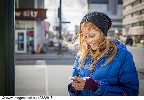 Junge Frau schreibt eine SMS auf ihrem Smartphone in der Innenstadt von Anchorage  Süd-Zentral-Alaska; Anchorage  Alaska  Vereinigte Staaten von Amerika