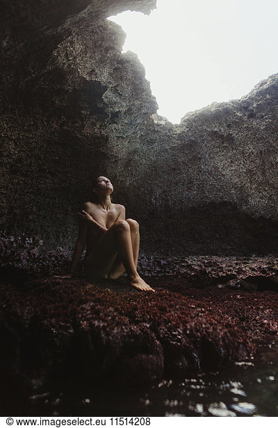 Junge Frau sitzt auf Felsen und schaut aus einer Höhle heraus  Mermaid Caves  Oahu  Hawaii  USA
