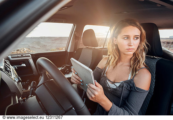 Junge Frau sitzt im Fahrzeug  hält ein digitales Tablet und schaut aus dem Fenster  Mexican Hat  Utah  USA