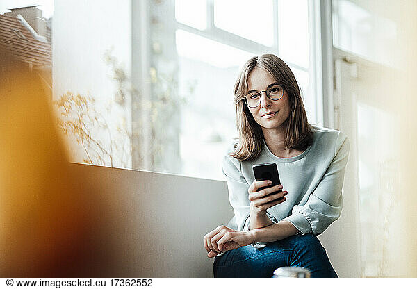 Junge Frau sitzt mit Mobiltelefon in einem Café