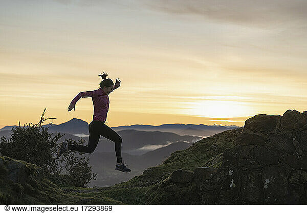 Junge Frau springt beim Laufen während des Sonnenaufgangs