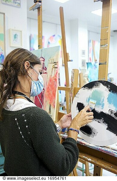 Junge Frau steht im Atelier und arbeitet an einem Bild.
