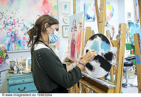 Junge Frau steht im Atelier und arbeitet an einem Bild.