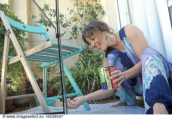 Junge Frau streicht einen Stuhl auf ihrer Terrasse grün an