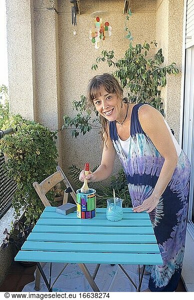 Junge Frau streicht einen Stuhl auf ihrer Terrasse grün an