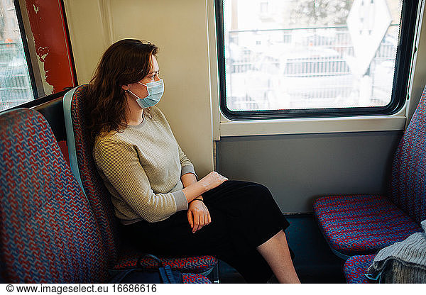 Junge Frau trägt eine medizinische Maske  während sie in einem Transportmittel sitzt