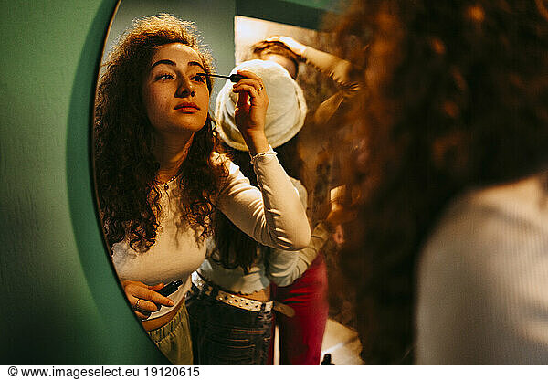 Junge Frau trägt Wimperntusche auf und schaut in den Spiegel