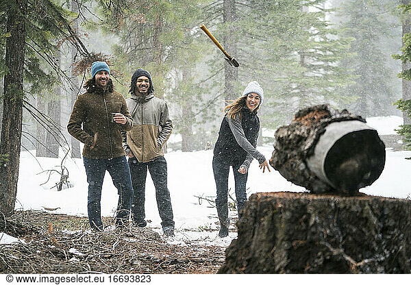 Junge Frau wirft Axt auf ein Ziel im verschneiten Wald  während ihre Freunde zusehen