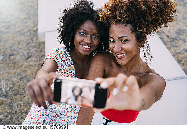 Junge Frauen  die lächeln und sich mit ihrem Smartphone in einem Park ein Selfie machen  Fokus auf den Hintergrund