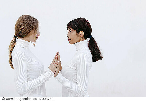 Junge Frauen  die sich an den Händen fassen und sich gegenseitig anschauen  vor weißem Hintergrund