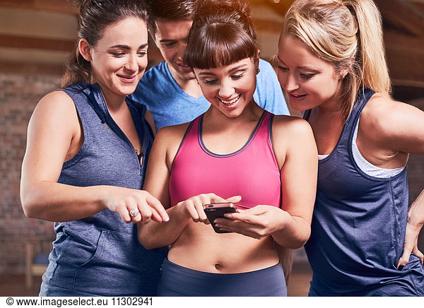 Junge Frauen und Männer in Sportbekleidung SMS mit Handy