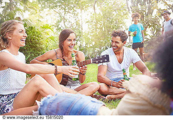 Junge Freunde  die lachen  abhängen  trinken und im Sommerpark Gitarre spielen
