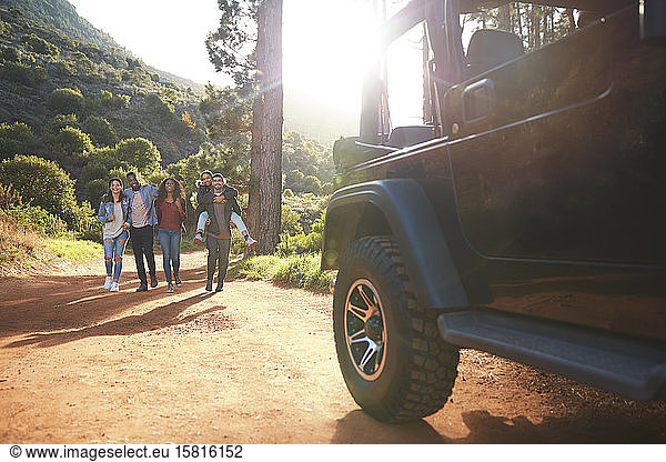 Junge Freunde gehen auf einem sonnigen Feldweg im Wald auf einen Jeep zu