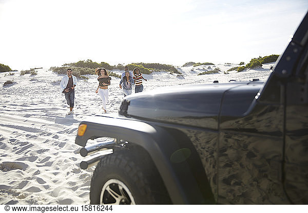Junge Freunde laufen am sonnigen Strand in Richtung Jeep