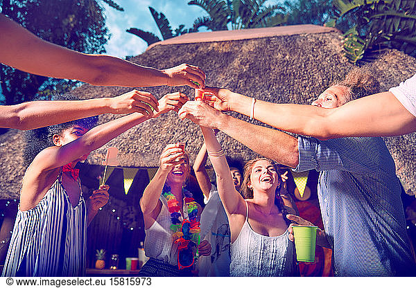Junge Freunde stoßen mit Alkohol in Schnapsgläsern auf einer Party am Pool an